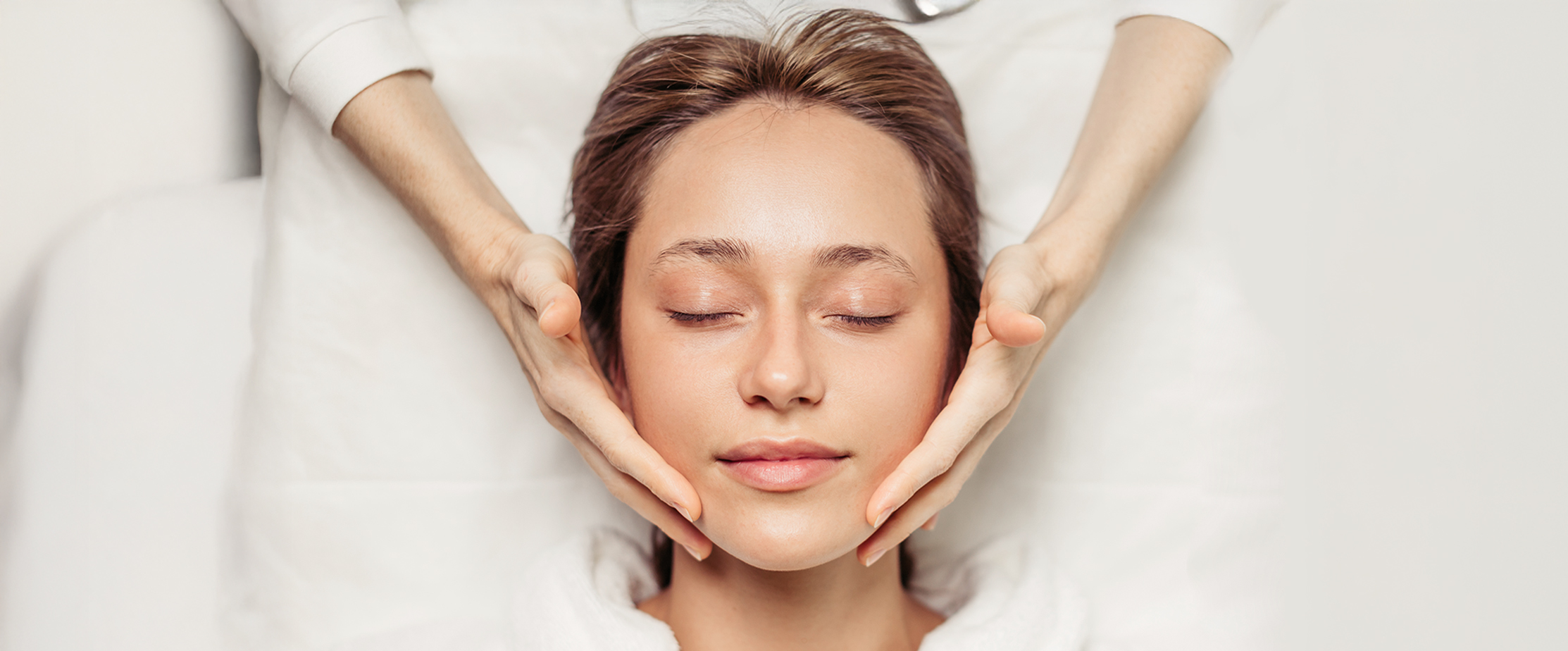 awesome young woman with closed eyes enjoying face massage in the spa center